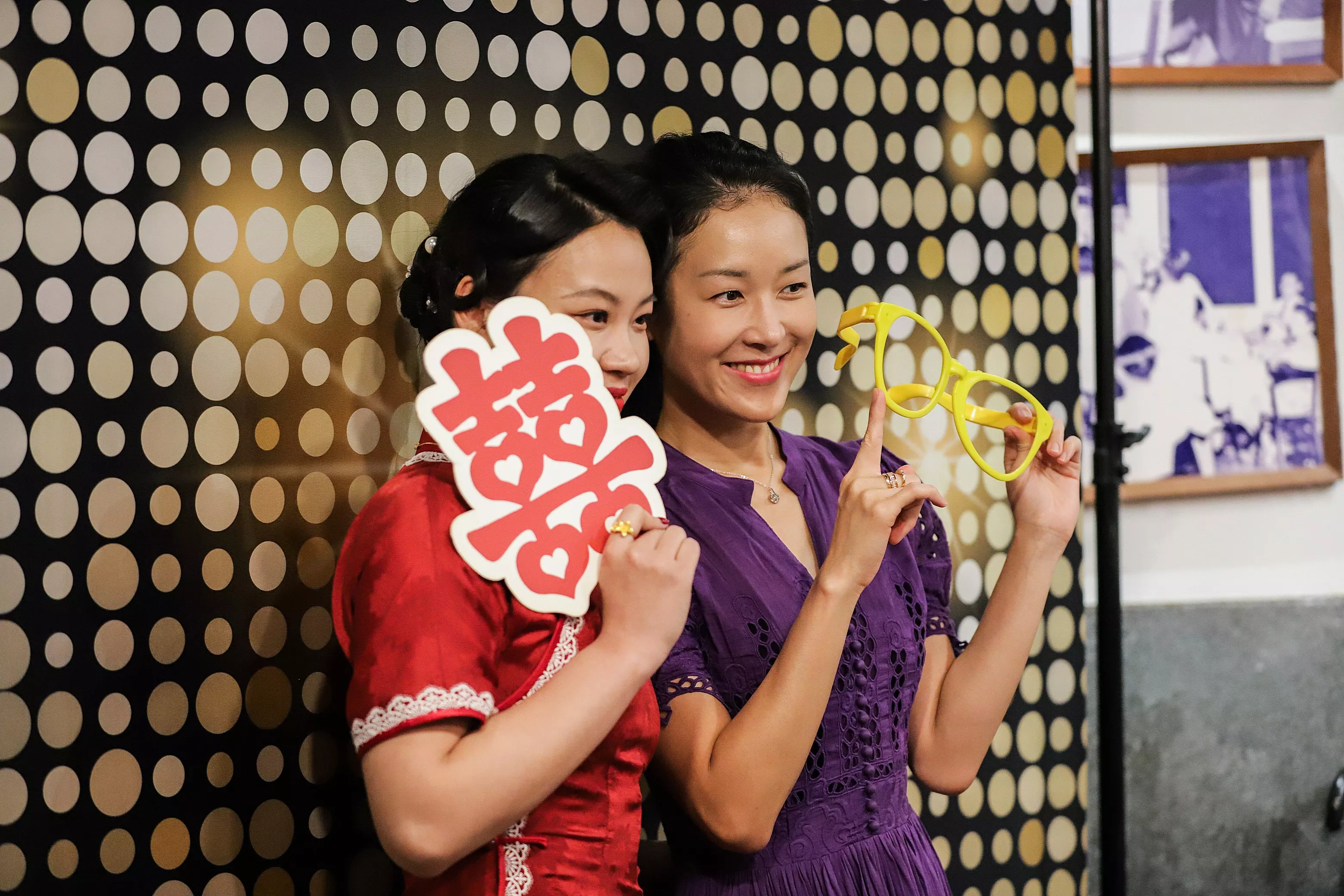 Two wedding guests posing playfully with prop signs at a photobooth backdrop
